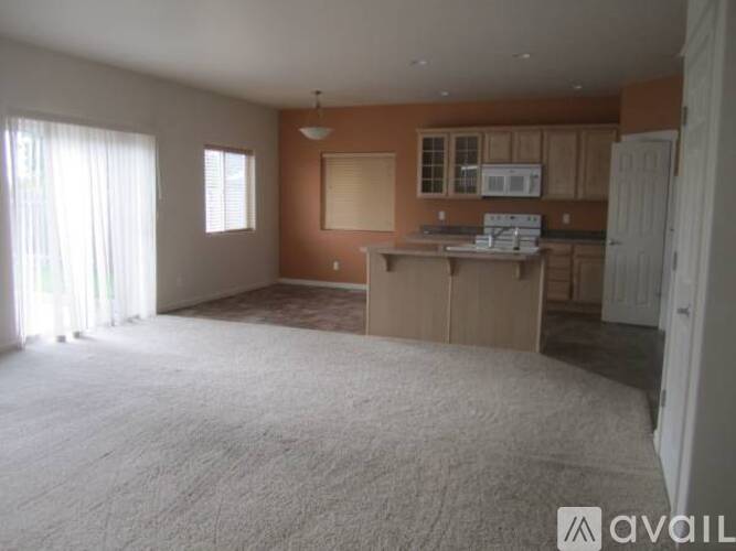 A room with a carpeted floor and a kitchen area in the background.