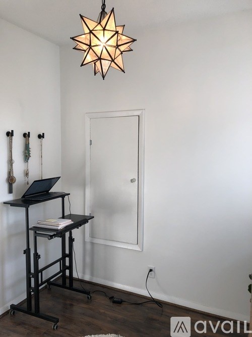 A black laptop is on a black rolling desk with a star-shaped light hanging from the ceiling.