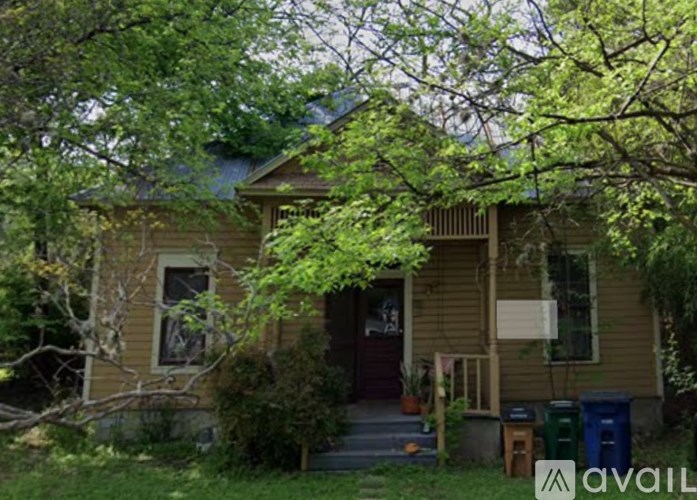 A house with a brown siding and a red door is surrounded by trees.