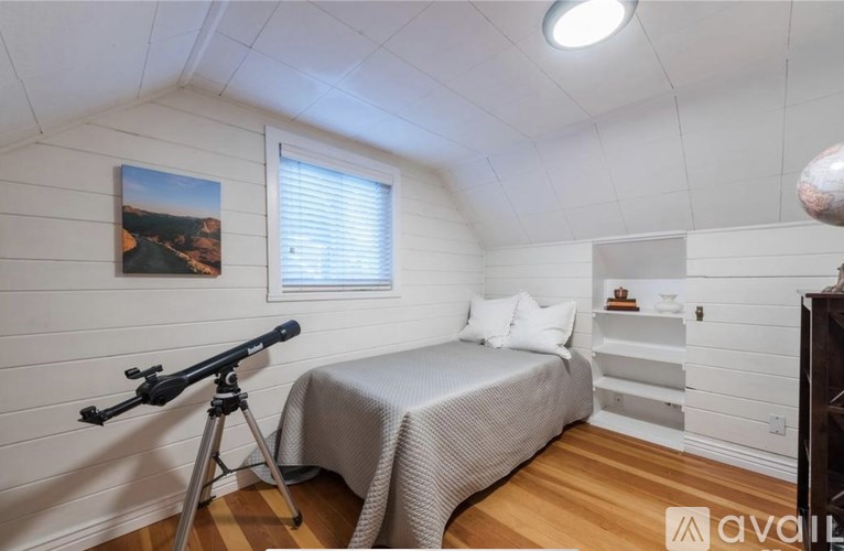 A bedroom with a bed, a tripod, and a picture on the wall.