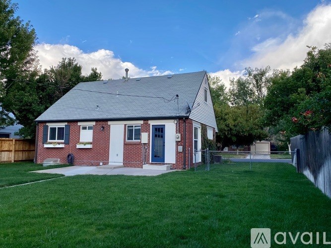 A house with a grey roof and a white door is surrounded by a green lawn.