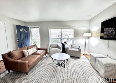 A living room with a brown couch, a grey armchair, a white ottoman, and a round table with a lamp on it.