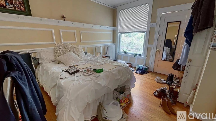 A bedroom with a bed covered in white bedding and a pile of shoes on the floor.