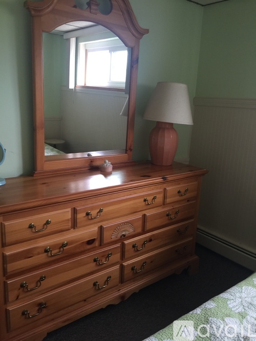 A wooden dresser with a mirror and a lamp on top.