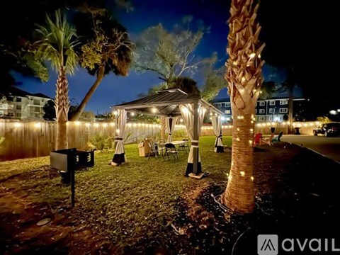 A gazebo is surrounded by palm trees and a fence with lights on it.