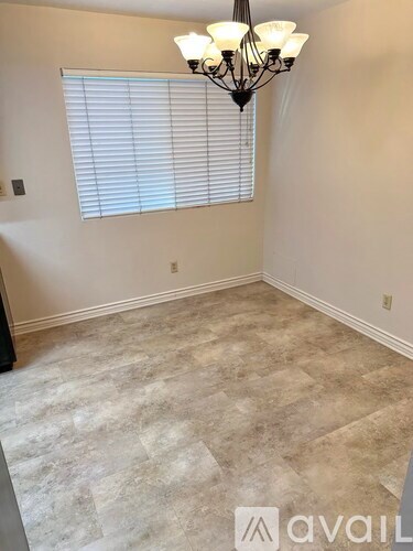 A room with a chandelier, a window with blinds, and a carpeted floor.