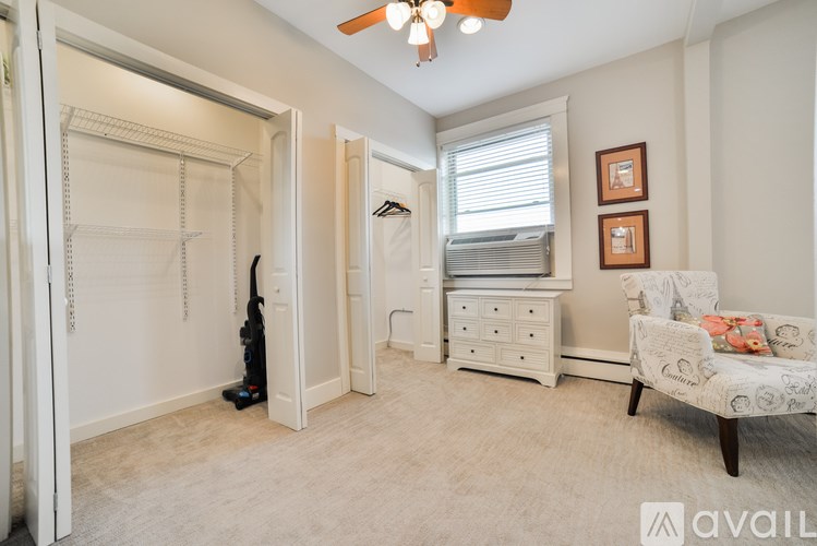 A room with a white chair and a white dresser with a window above it.