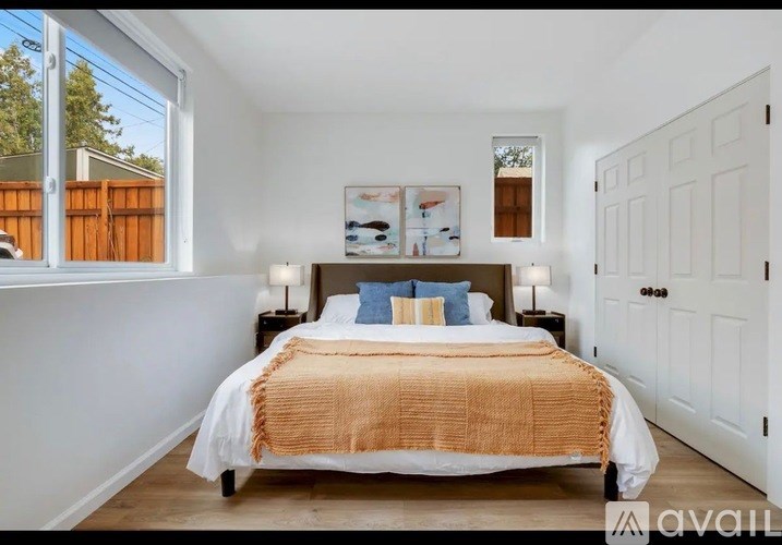 A bedroom with a bed, two lamps, and a window overlooking a fence.