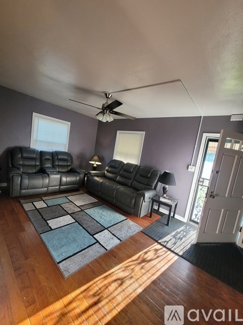 A living room with a black leather sofa and a wooden floor.