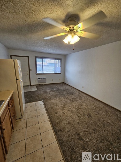 A room with a ceiling fan and a kitchen area with a refrigerator.