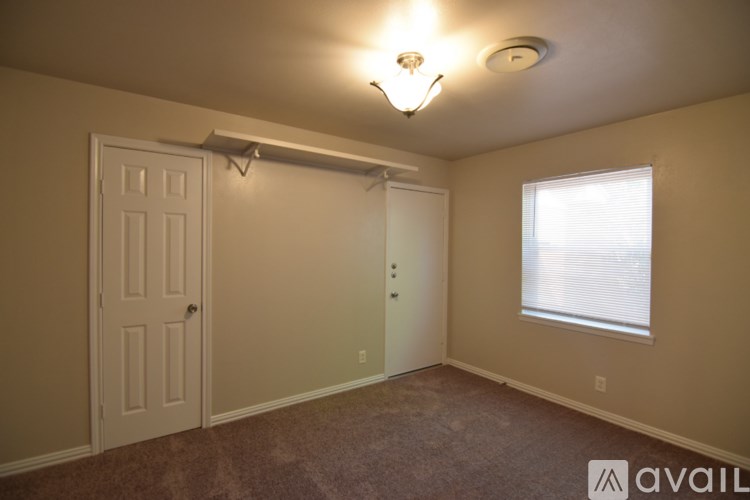 A room with a carpeted floor, a window with blinds, a white door, and a light fixture on the ceiling.