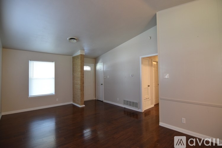 A large empty room with wooden floors and a brick wall on the left side.