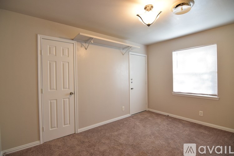 A room with a carpeted floor, a window with blinds, and a light fixture on the ceiling.