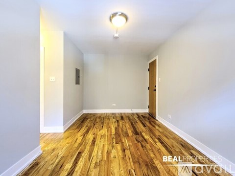 A room with wooden flooring and white walls, with a light on the ceiling and a door on the right.