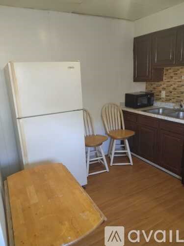 A kitchen with a white fridge, brown chairs and a wooden table.