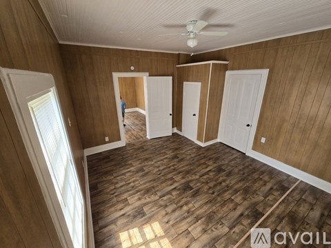 A room with wooden walls and floors, a ceiling fan, and a window letting in natural light.