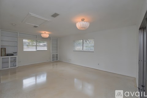 A spacious room with a white ceiling and floor, two windows with blinds, and a light fixture hanging from the ceiling.