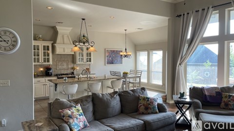 A living room with a grey couch and a kitchen area in the background.