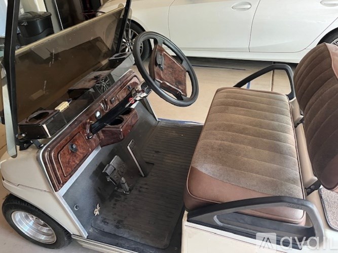 A white golf cart with brown seats and a wooden steering wheel.