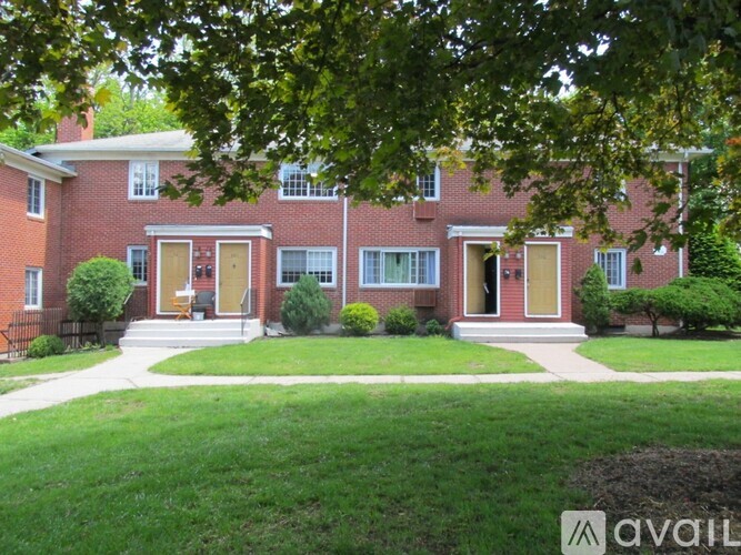 A red brick house with a front yard and a tree in the foreground.
