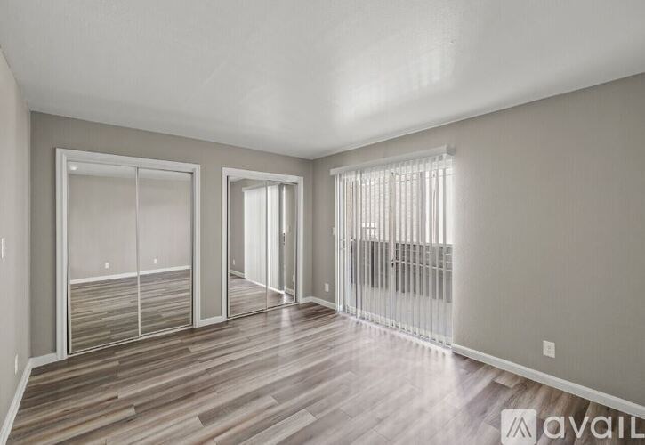 A spacious room with wooden flooring and a large window with blinds.