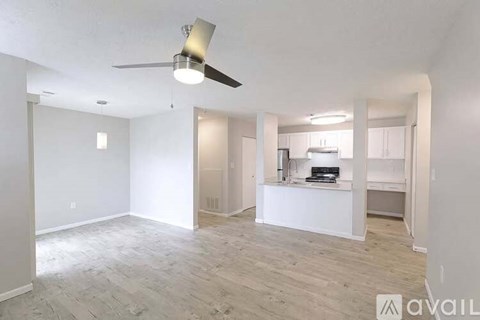 A spacious room with a ceiling fan and a kitchen area in the background.