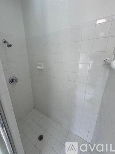 A white tiled shower with a drain in the middle.