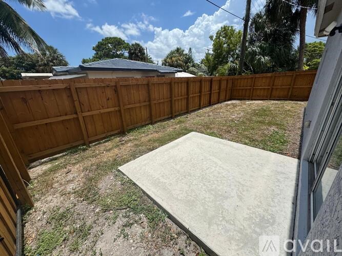 A backyard with a wooden fence and a concrete slab in the foreground.