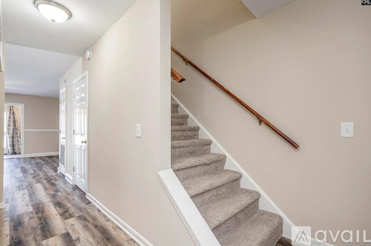 A staircase with a wooden handrail and beige carpeted steps.