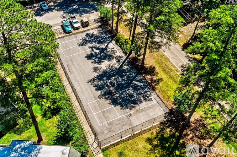 A tennis court surrounded by trees and a parking lot.