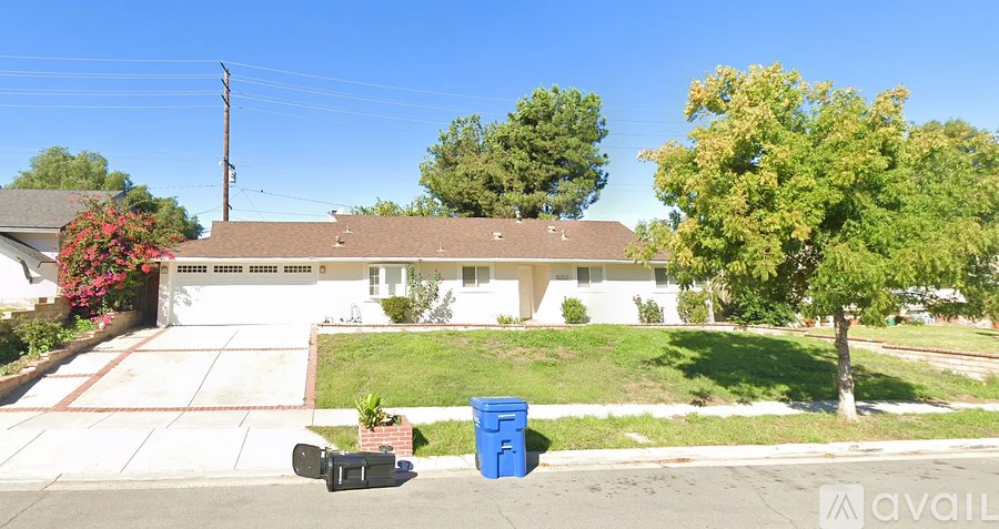 A house with a blue trash bin in front of it.