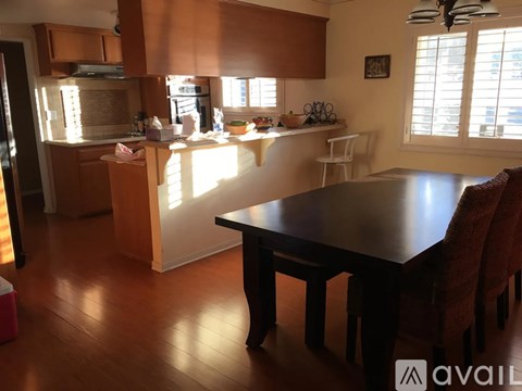 A kitchen with a table and chairs in the foreground and a counter with a sink and a window in the background.