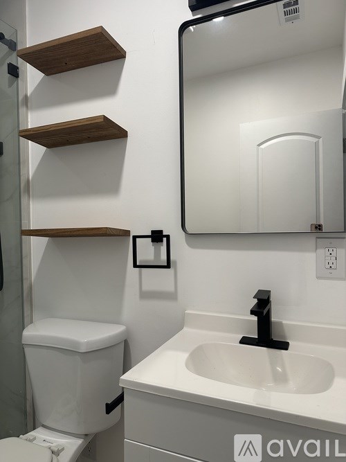A white toilet with a black flush handle is next to a white sink with a black faucet.
