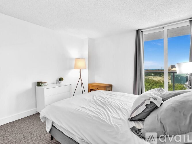 A bedroom with a large bed, a nightstand with a lamp, and a window with a view of the outside.