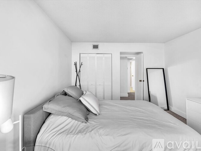 A white bedroom with a bed, nightstand, and lamp.