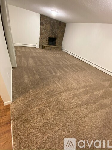 A room with a carpeted floor and a stone fireplace.