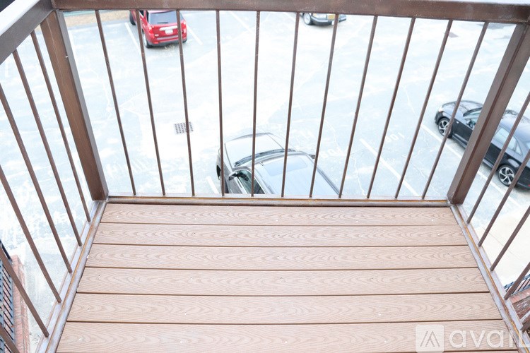 A balcony with a wooden floor and railing overlooking a parking lot with cars.