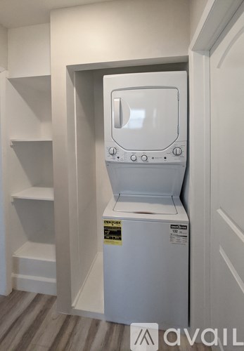 A white washing machine is in a small space between a wall and a door.