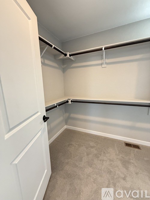 A white door is on the left side of a room with a carpeted floor and a shelf on the right.