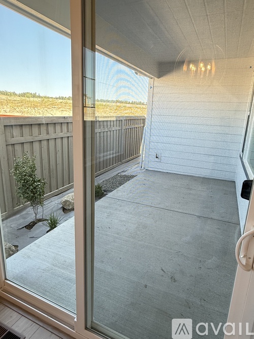 A balcony with a glass door and a view of a fence and trees.