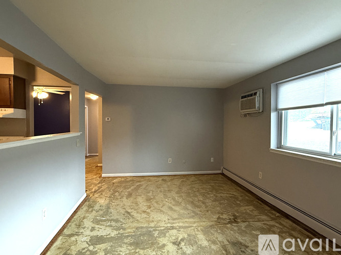 A room with a carpeted floor, a window with black curtains, and a wall-mounted air conditioner unit.