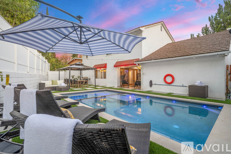 A pool with a white umbrella and chairs.