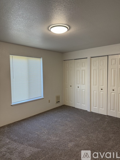 A room with a carpeted floor, a window with blinds, and a ceiling light fixture.