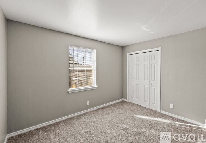 A room with a carpeted floor, a window with blinds, and a white door.
