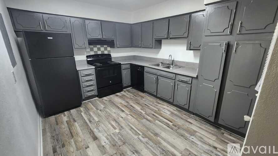 A kitchen with black appliances and wooden flooring.