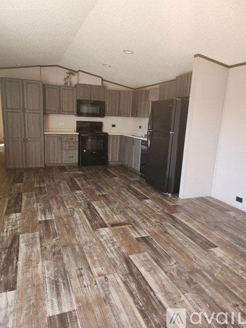 A kitchen with wooden flooring and a black fridge.