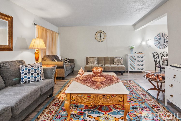 A living room with a grey couch, a wooden coffee table, and a rug with a multicolored pattern.