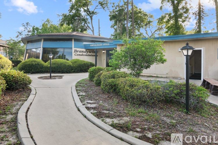 A building with a sign that says "Brandywine Condominiums" is surrounded by bushes and trees.