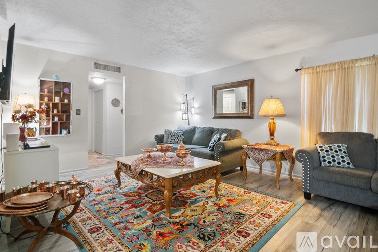 A living room with a grey couch, a wooden coffee table, and a rug with a multicolored design.