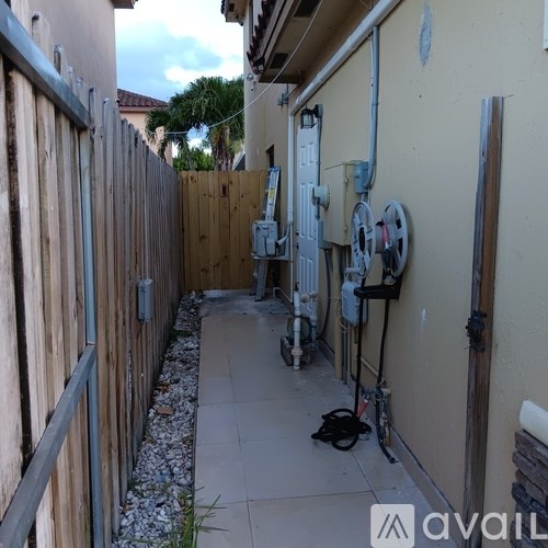 A narrow alley with a wooden fence on the left and a wall with electrical boxes on the right.
